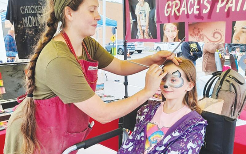 Grace Johnson paints the face of Mercy Lenihan at the Murphy Spring Festival in May 2022. Youngsters patiently waited in line to receive one of her creative and fun designs. 