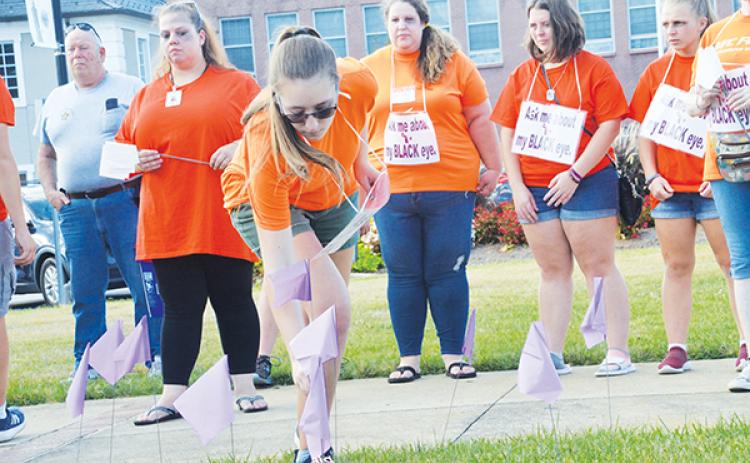 Jasmine Weaver plants a flag in remembrance of victims who died as a result of domestic violence. In rear wearing orange are Jessica Vernon, Stacy Van Buskirk, Lilli Johnson and Allana Johnson (from left).