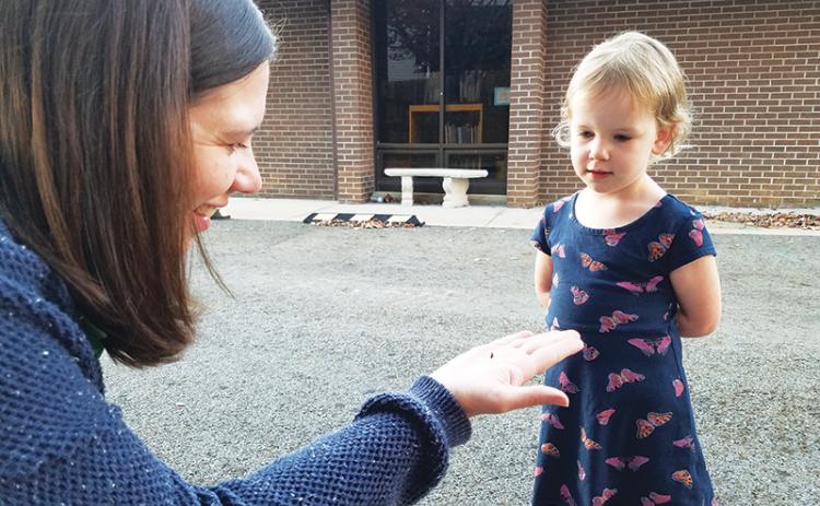 North Carolina Arboretum ecoExplore coordinator Libbie Dobbs-Alexander explains to 3-year-old Cora Dance of Murphy that the bug she found on the library grounds is a ladybug larva.