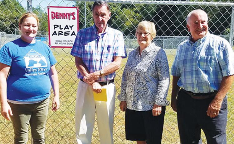 Animal shelter manager Kirsty Waller and Valley River Humane Society President Jeff Manson reveal the sign reading "Denny's Play Area" to its namesake, Denny Kendall, and his wife, Diane. 