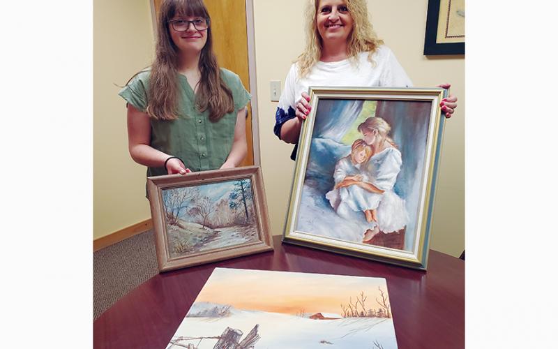 Marlee Postell (left) and her mother, Angie Holland, hold paintings done by three generations of women in their family. The landscape Marlee is holding is her great-grandmother’s Dot Pullium, Angie is holding a portrait by her mother, Diane Mintz, while Angie’s landscape lays in front of them.