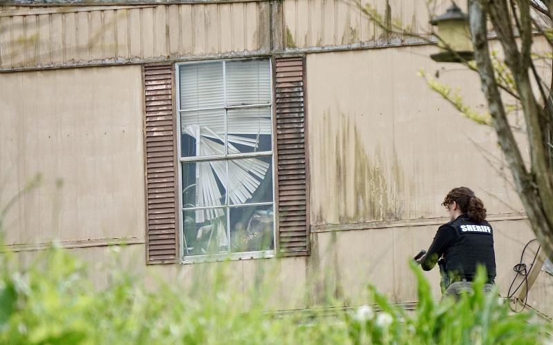 An unidentified sheriff's detective, with gun drawn, covers a window during a standoff on Fort Butler Street in Murphy on Thursday, April 13, 2023.