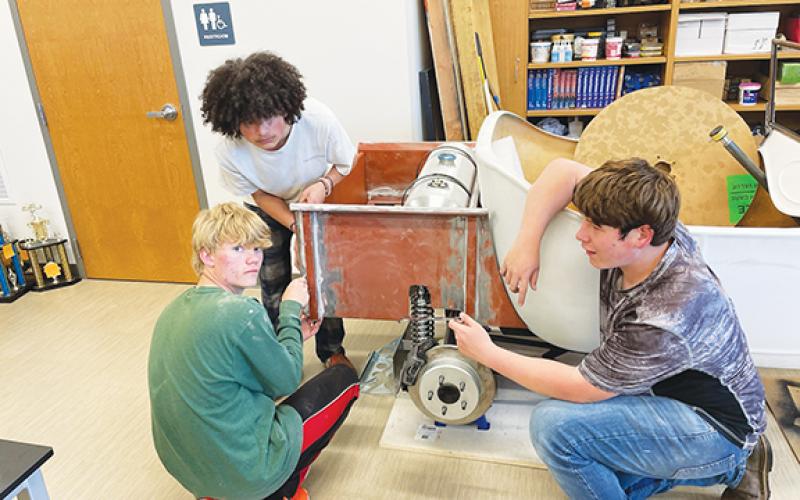 Students help build a car kit in John Worden’s class at The Oaks Academy in Peachtree. Eli Conley (wearing green), Zaylen Allen (in white) and Hunter VanMeter (right) work on test fitting the handmade bed for the T-bucket project.