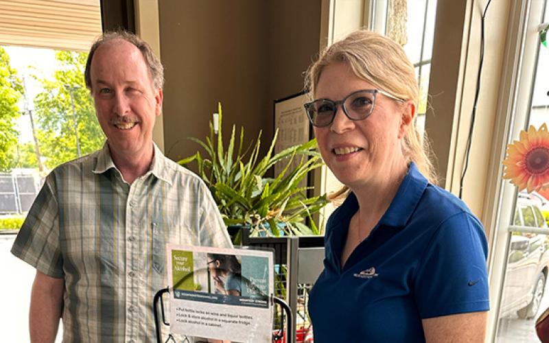 Waynesville ABC staff photo Waynesville ABC store manager Mark Strugnell (left) welcomes Mountain Projects Prevention Manager Libby Ray as she places a display rack for alcohol locks. Mountain Projects gave away more than 1,500 free locks for bottles, cabinets and refrigerators around western North Carolina in 2025. This prevention strategy is meant to reduce access to alcohol for those who are underage.