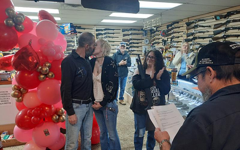 Anngee Quinones-Belian/Staff Correspondent Odin Kamrow and Holly Garrett kiss for the first time as a married couple Saturday as bridesmaid Kahla Ivester looks on. Ivester holds the gifted shotgun from Cherokee Guns. Bob Murray, minister on staff, married the couple.