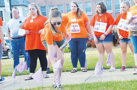 Jasmine Weaver plants a flag in remembrance of victims who died as a result of domestic violence. In rear wearing orange are Jessica Vernon, Stacy Van Buskirk, Lilli Johnson and Allana Johnson (from left).