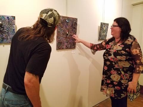 Marie Gunther points out shotgun shells used in her three dimensional piece "Through a Glass Darkly" to Tom Vogler. The piece was on display at the Andrews Art Museum on the second floor of the Valleytown Cultural Arts Center during Writers & Wine.