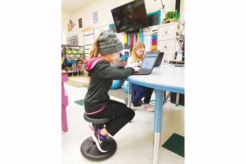 Rylei Howard (hat) and Bella Kent sit on wobble stools – a supply their teacher would like more of – while Dylan Adams and Joe Payton Moses (background) sit on stability balls to work on their Chromebooks. Photo by Samantha Sinclair