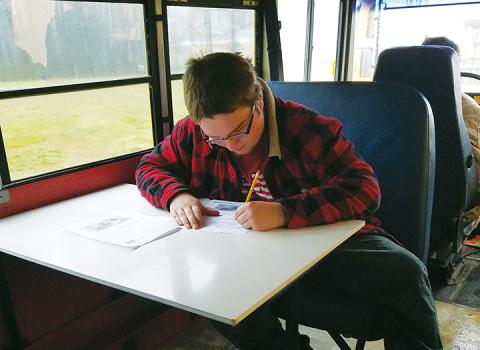 Andrew Graves uses one of the tables at the front of the former Bus 101 to complete classwork. Photo by Samantha Sinclair