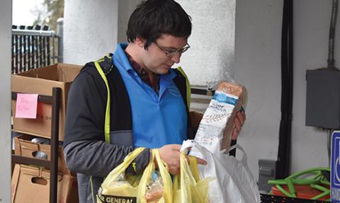 Volunteer Christopher T. Beaver II carries bags of food to a family’s car on March 17 during the initial run of the Sharing Center food pantry’s drive-through service. Photo by Samantha Sinclair