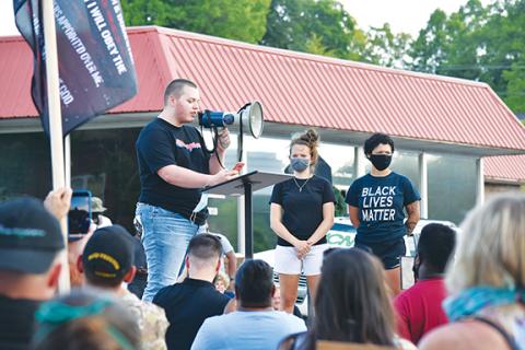 As Emily Mills and Te’Lor Allen stand beside him on the stage, Jake Reed addresses the crowd gathered near the Cherokee County Courthouse during the protest they organized Thursday. Photo by Samantha Sinclair