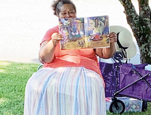 Abigail Hickman/Staff Correspondent Patricia Hall, president of One Dozen Who Care, reads from a book on the lawn of the Murphy Public Library during their 2021 summer story-time series. 