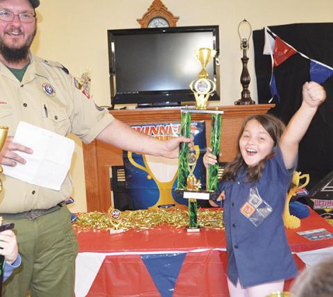 Photos by Abigail Hickman/Staff Correspondent Top photo: Haylee Reinhardt bursts with pride at her first-place trophy. Left photo: Haylee smiles confidently before the race with her winning entry, The Awesome Blue Jeep, at the annual Pinewood Derby on Saturday.
