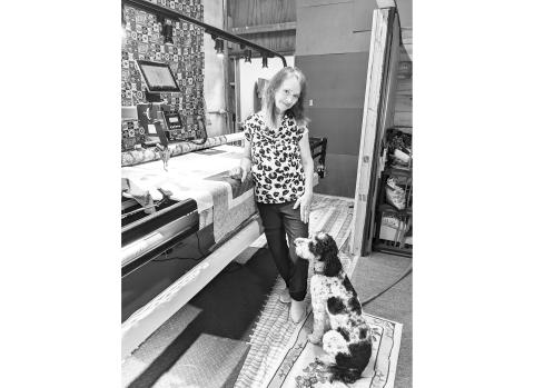 Rachel Carr stands at her long arm quilting machine with her “shop dog” Ziggy.