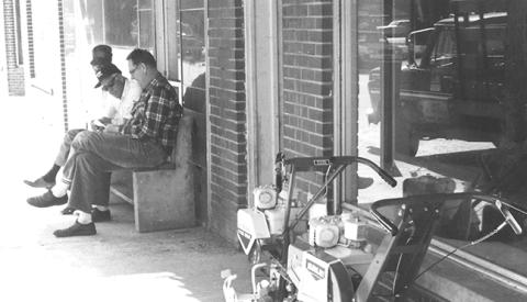 For many years Charles Freel would sit on the bench outside his furniture store on Main Street and visit with the locals who stopped by. It was like a scene in a Norman Rockwell painting. Sitting beside him is Jack Ledford, but the writer could not identify the next man. You can tell it was a nice spring day, as the garden tillers were displayed on the sidewalk. 