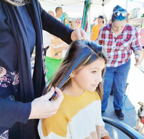 Laura Ledford with Images Salon adds shiny tinsel to the hair of Lexi Crisp on Saturday at the annual Oktoberfest event in downtown Andrews.