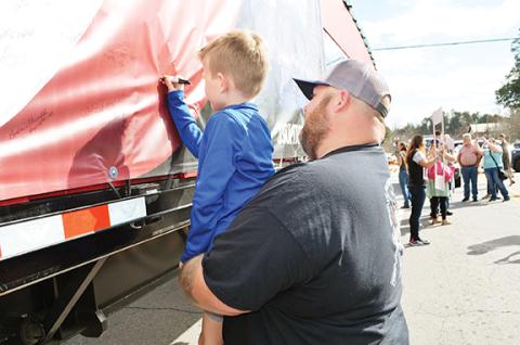 Photos by Abigail Blythe Batton/Staff Correspondent Top: Colt Allen, 6, of Hayesville, gets a boost from his dad, Dwayne Allen, to sign his name to the U.S. Capitol Christmas Tree truck card Sunday in Murphy