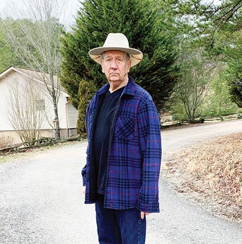 Abigail Blythe Batton/ Staff Correspondent  David Grimes stands at the point where pavement ends and gravel starts at the Wells Lake subdivision in southern Cherokee County.