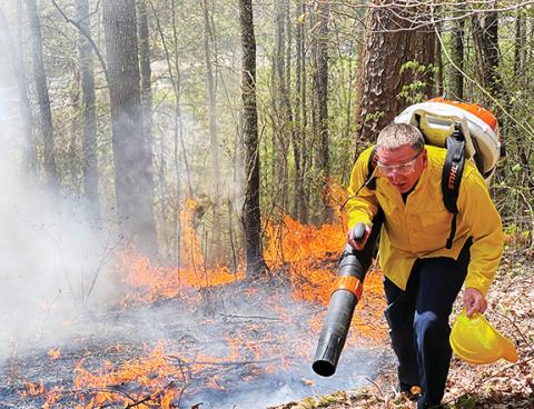 Photos by Randy Foster/editor@cherokeescout.com   Above: An area firefighter uses a high-powered leaf blower to push the flames back onto themselves during a woods fire off of Joe Brown Highway on Thursday afternoon. 