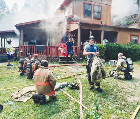 Randy Foster/editor@cherokeescout.com Firefighters catch their breath Thursday after searching a burning house at 505 Haywagon Lane in west Cherokee County. A firefighter brings a child’s rocking horse out of the damaged building to give to residents of the house.