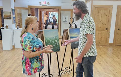 Nicole Wright/Staff Correspondent Artist Emory Nolan (right) discusses his painting “Dandy Dandies” with newly appointed Cherokee Chamber of Commerce ambassador Winkie Styles (left) while attending the chamber’s After Hours event Friday at the Cherokee County Arts Council in downtown Murphy. While Nolan has been in the area for two years, Styles has been in the area for 22 years.
