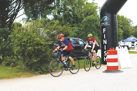 Photos by Cannon Crompton/sports@cherokeescout.com Above: Rod Fortney (left) of Murphy and Charles Curtis (right) of Roswell, Ga., start their 16-mile warmup loop Friday afternoon at the Cycle NC Mountain Ride. Below: A sign welcoming cyclists to Konehete Veterans Park in Murphy.