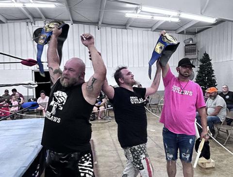 The American Outlaws, Killshot (left) and Axel Freakin Gunn (right), hold their belts after successfully defending them Saturday night at the Peachtree Community Center. They are joined by Kevin Seiber (middle).