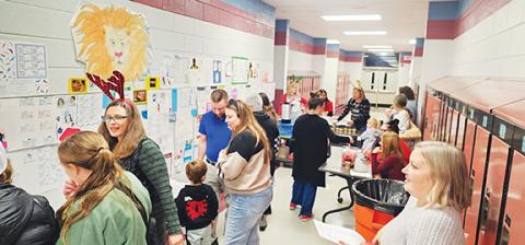 Photos by Nicole Wright/Staff Correspondent Science teacher Bethany Clark (left, in plaid reindeer ears) stands with students and staff and families in front of her classes’ poster board Punnett square projects during Andrews Middle School’s Winter Art Showcase of students’ academic and artistic projects.