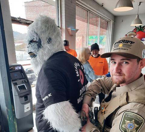 Photos by Anngee Quinones-Belian/Staff Correspondent Left: The Abominable Doughman (Scott Crawford) with Crafted Dough was taken into custody by Cherokee County sheriff’s Deputy Jake Worrell on March 7. The arrest could have gone south quickly, but Worrell maintained control of the creature. Right: Rotary Club of Murphy President Jacky Egli probably didn’t realize that offering Sheriff Dustin Smith a donut to avoid the consequences is a crime, but at least she did it with a smile at Downtown Pizza.