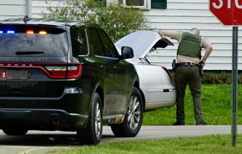 A sheriff’s deputy, hand on his sidearm, checks a trunk on Airport Road. 