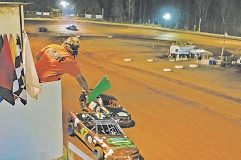 Cannon Crompton/sports@cherokeescout.com Jeremy Maples waves the green flag to restart the Front-wheel Drive race after a yellow flag at Tri-County Racetrack on April 18. Drivers Phillip Hall of Andrews (No. 47, left) and Shannon Jones of Hayesville (No. 32, right) are shown racing down the track below Maples.