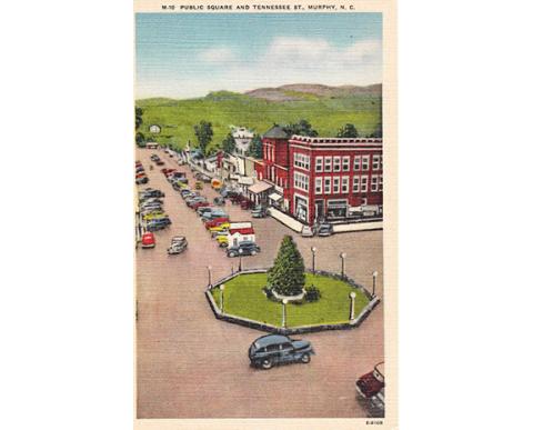 A pre-1917 postcard showing the Bull Moose Pen roundabout in downtown Murphy. A fountain would replace the evergreen in 1917 – a fountain that today rests in front of the Cherokee County Historical Museum.