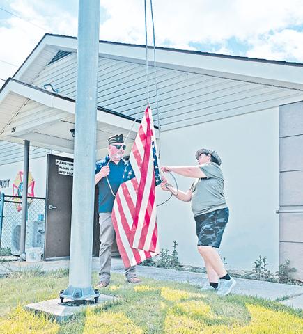 Photos by Nicole Wright/Staff CorrespondentSenior vice commander Candis Browand (right) and former post commander and chaplain JD Baker hoist the annual single flag representative of the many others to be incinerated during Andrews VFW Post 7620's annual flag retirement ceremony on June 14.