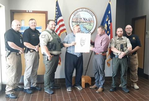 Photos by Anngee Quinones-Belian/Staff Correspondent  Sheriff Dustin Smith and members of the Cherokee County Sheriff’s Office accepted the heartfelt gift of a sketch drawing of Officer Francisco Flattes on Aug. 27. From left are David Williams, patrol captain; Justin Jacobs, chief deputy; Hunter Cornwell, deputy; Mike Lalone, artist; Sheriff Dustin Smith; Robert Manning, deputy; and Brian Smith, captain over the Cherokee County Detention Center, where Flattes worked.