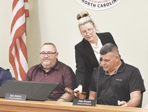 Randy Foster/editor@cherokeescout.com Commissioner Ben Adams (left) looks on as board clerk Maria Hass passes the chairman’s gavel to Alan Bryant during Monday night’s Cherokee County Board of Commissioners meeting. The Dec. 1 meeting was held two weeks early in order to establish the board’s organization going into 2026. Story, page 9A.
