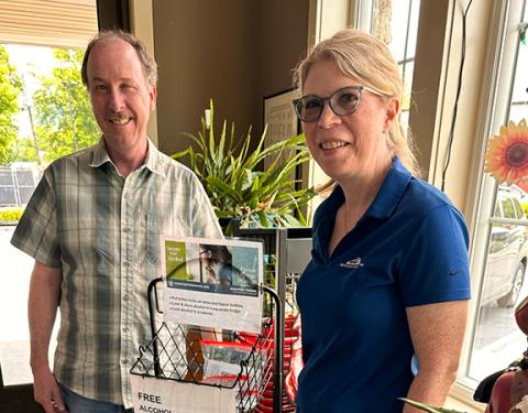 Waynesville ABC staff photo Waynesville ABC store manager Mark Strugnell (left) welcomes Mountain Projects Prevention Manager Libby Ray as she places a display rack for alcohol locks. Mountain Projects gave away more than 1,500 free locks for bottles, cabinets and refrigerators around western North Carolina in 2025. This prevention strategy is meant to reduce access to alcohol for those who are underage.