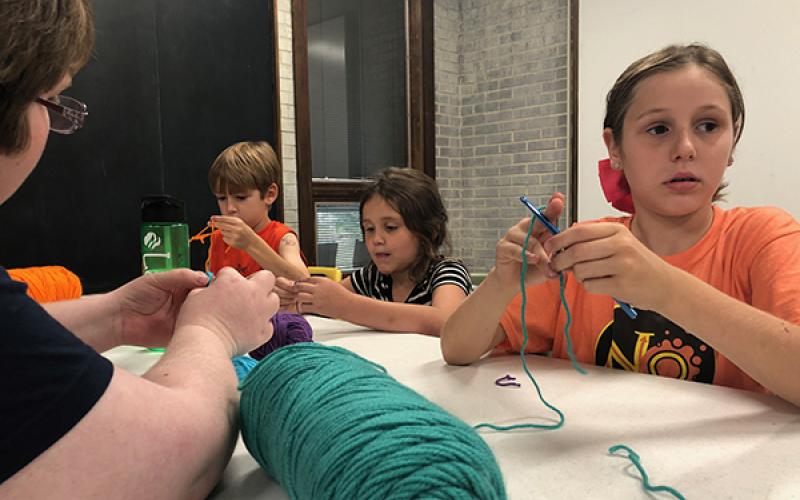 Zander Vaught, 8, Lacie Hall, 7, and Kimber Vaught, 9, learn crochet techniques taught by Bridget Wilson at the Andrews Public Library. 