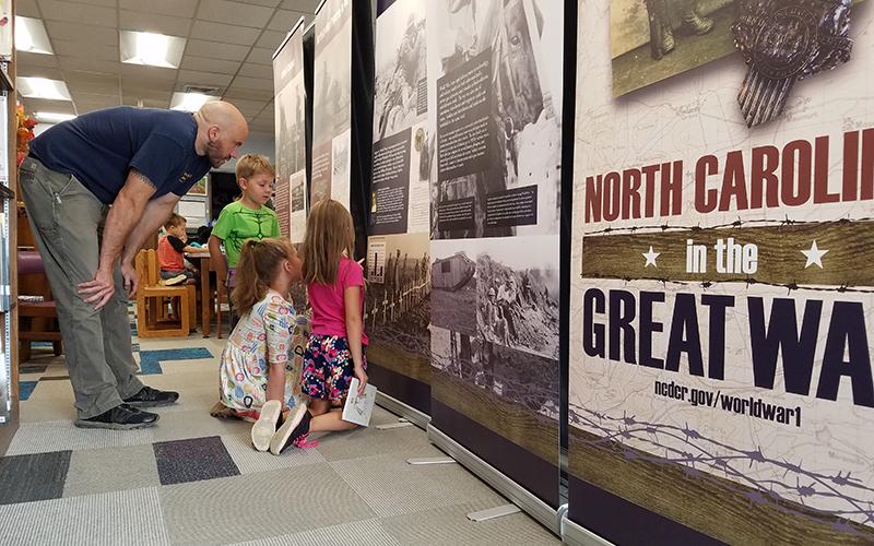 Andrew Gray helps Austin Gray, 6, Rowan Woods, 7, and Callie Gray, 7, understand the North Carolina in the Great War exhibit after storytime at the Andrews Public Library.