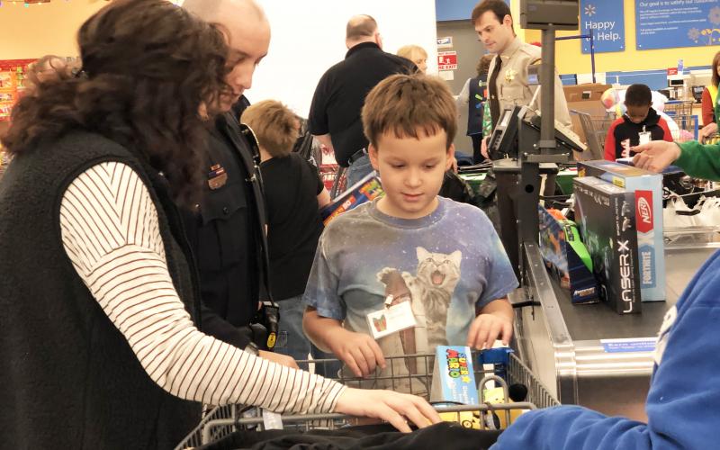Zachary Gent admires the basket full of toys he picked out during Shop With a Cop on Saturday morning at Walmart in Murphy. Photo by Penny Ray.