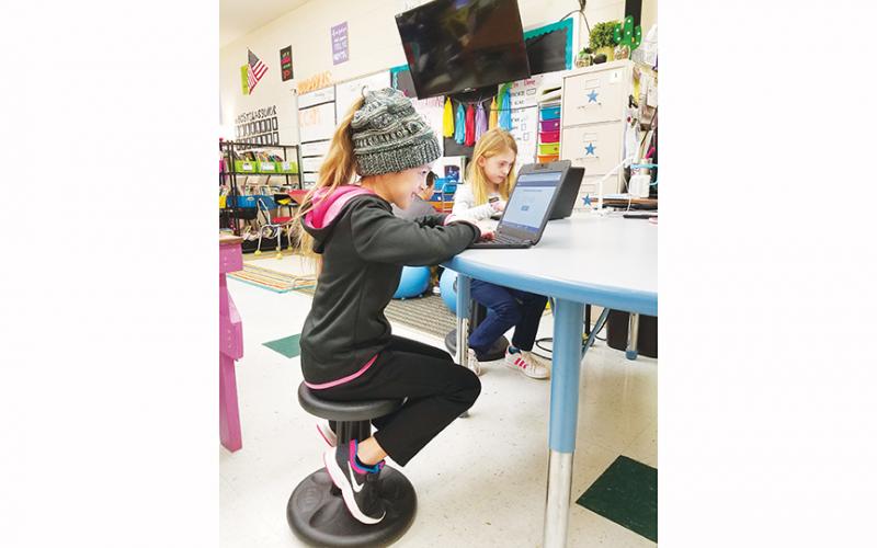 Rylei Howard (hat) and Bella Kent sit on wobble stools – a supply their teacher would like more of – while Dylan Adams and Joe Payton Moses (background) sit on stability balls to work on their Chromebooks. Photo by Samantha Sinclair