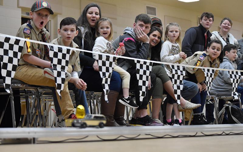 Families watch as two Pinewood Derby cars race past them. Photo by Samantha Sinclair