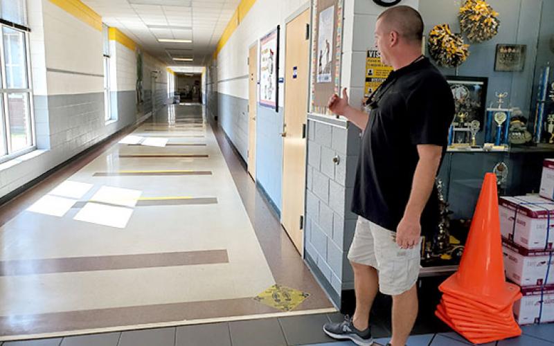 Murphy Elementary Principal Dane Rickett shows decals placed on the floors to remind children to maintain six feet of distance. Children will be told not walk in the center of the hallway within the yellow stripes. Photo by Samantha Sinclair