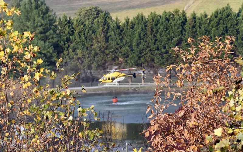A helicopter fills its bucket from a private pond off Pisgah Road Thursday evening. 