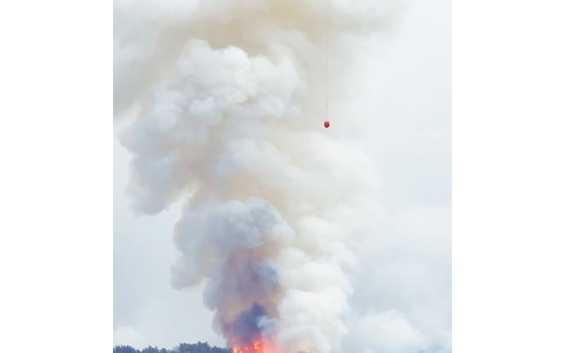 Photos by Randy Foster/editor@cherokeescout.com Above: A heavy-lift helicopter prepares to drop water from a bucket on a hot spot in the Collett Ridge Fire east of Pisgah Road on Thursday. At right: Smoke from the fire shrouds the morning sun off of Junaluska Road on Sunday. Full page of photos, 9A.