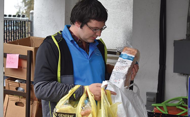 Volunteer Christopher T. Beaver II carries bags of food to a family’s car on March 17 during the initial run of the Sharing Center food pantry’s drive-through service. Photo by Samantha Sinclair