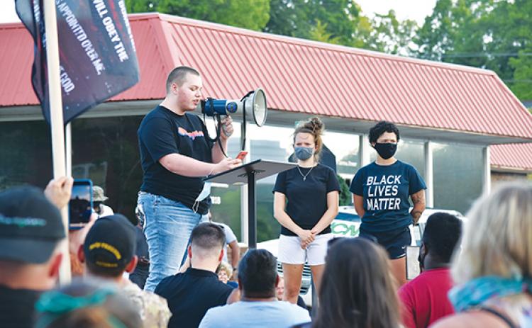 As Emily Mills and Te’Lor Allen stand beside him on the stage, Jake Reed addresses the crowd gathered near the Cherokee County Courthouse during the protest they organized Thursday. Photo by Samantha Sinclair