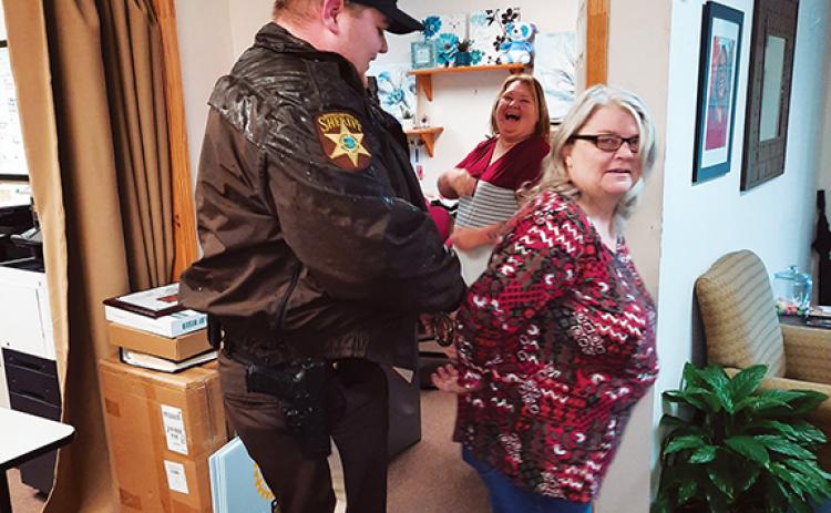 Anngee Quinones-Belian/Staff Correspondent Cherokee County sheriff’s Deputy Tim Leslie arrests Reach of Cherokee-Graham County Executive Director Cecilia Crawford-Faulkner on March 1 as Women’s Resource Center coordinator/court advocate Amanda Hamby looks on with what looks like lots of laughter.